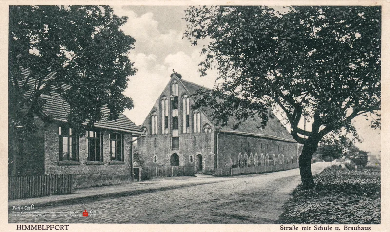 Eine schwarzweisse Ansichtskarte zeigt die Klosterstra&szlig;e Himmelpfort. Links die frisch erbaute Dorfschule, ein einst&ouml;ckiges Backsteingeb&auml;ude mit gro&szlig;en Bogenfenstern, dahinter das langgestreckte backsteingotische Brauhaus mit einem Ziergiebel, darauf ein Storchennest.